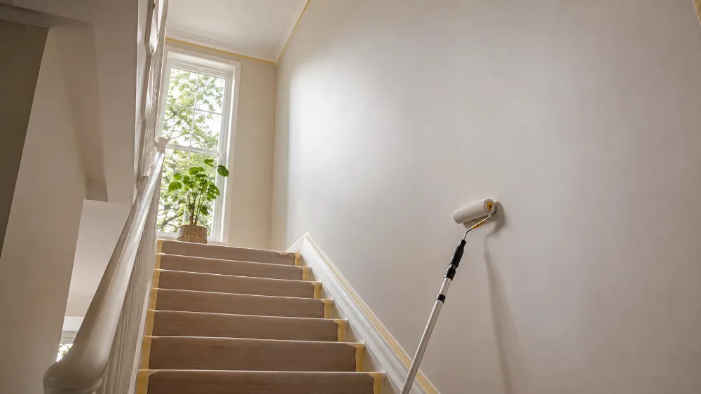 Helles Innen-Treppenhaus mit abgeklebten Kanten, geschützten Stufen und Farbrolle an der Wand